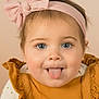 baby, child, tongue_out, headband, pink_bow, blue_eyes, mustard_outfit, ruffles, closeup, portrait, cute, smiling, infant, soft_background, adorable, happy, wearing_clothes, face, expression, indoor