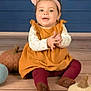 Camila is registered to the contest to win money with this photo: baby, child, girl, clapping, headband, bow, mustard_dress, maroon_leggings, plush_pumpkins, wooden_floor, blue_wall, smiling, happy, sitting, indoor, cute, portrait, infant, playful, cozy