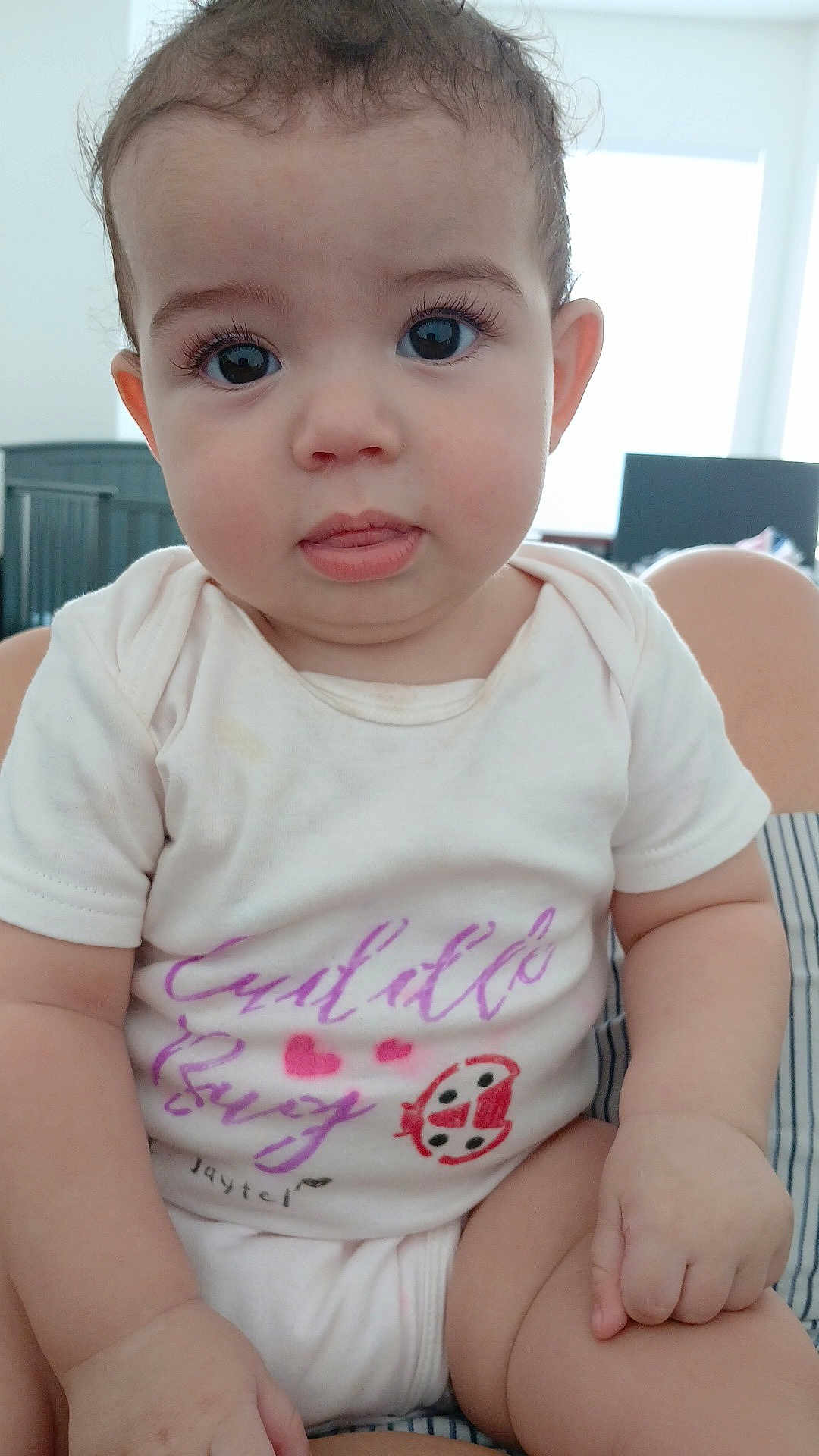 Addison joined the competition — help win amazing prizes! baby, infant, child, onesie, sitting, cute, indoor, curious, face, hands, legs, ladybug, clothing, window, crib, expression, skin, eyelashes, person, portrait