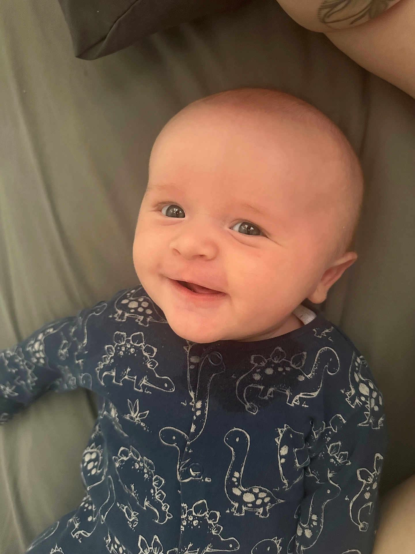 Cody is registered to the contest to win money with this photo: baby, smiling, onesie, dinosaur_pattern, infant, face, cute, happy, child, portrait, closeup, lying_down, soft_light, indoors, person, apparel, young, skin, head, expression