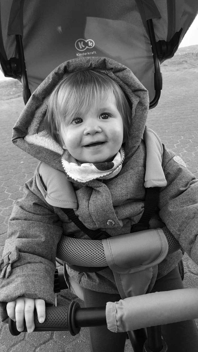 Maëlys participe au concours pour gagner de l'argent avec cette photo : child, toddler, smile, jacket, hood, scarf, stroller, handlebar, outdoor, pavement, black_and_white, happy, portrait, baby, person, cute, winter_clothing, young, face, grip