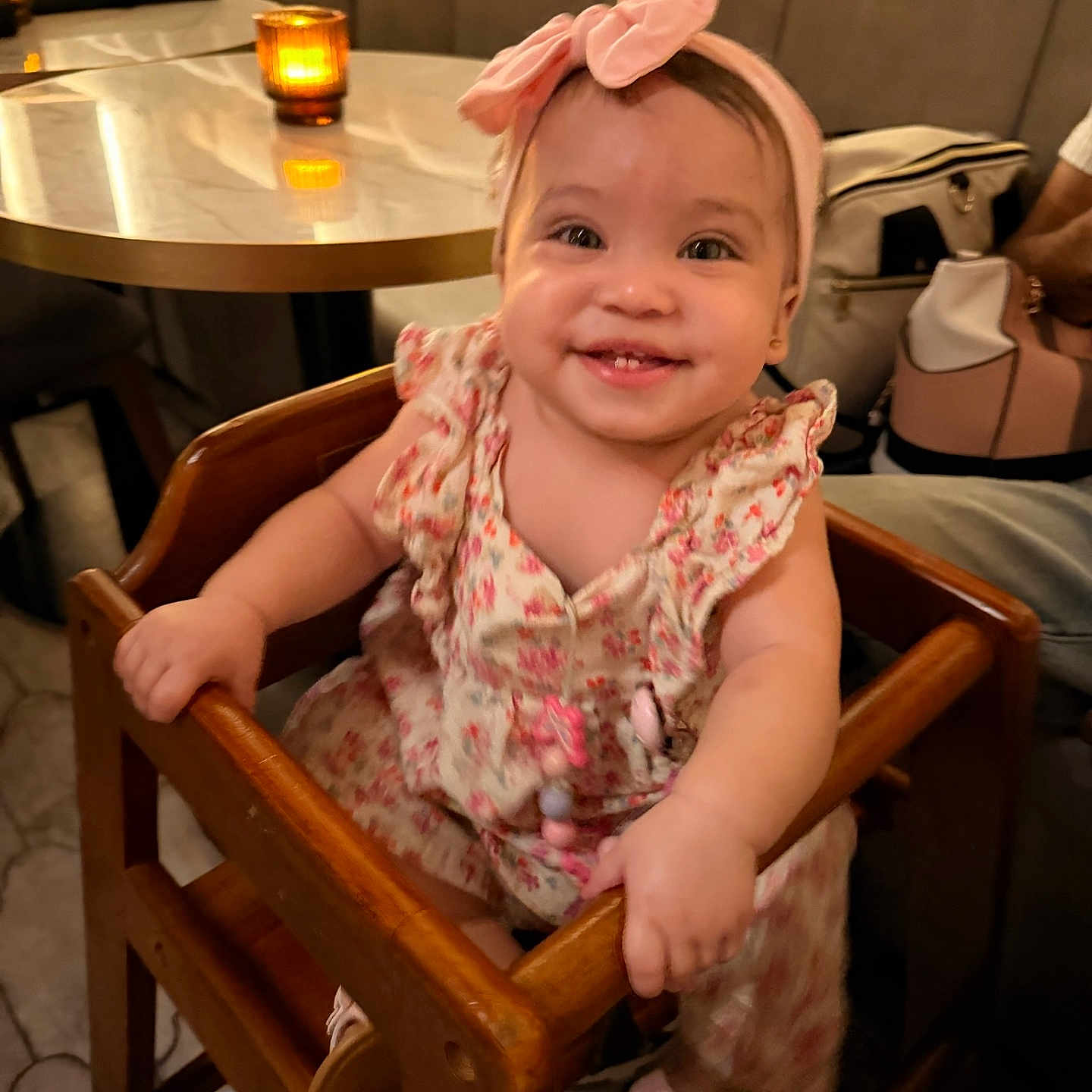 Jhaslyn is registered to the contest to win money with this photo: baby, child, smiling, happy, portrait, indoors, restaurant, high_chair, pink_bow, headband, floral_dress, sitting, wooden_furniture, table, candlelight, dinner, background, infant, toothy_smile, family_dining