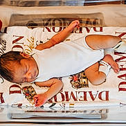 Daemon King Vela is registered to the contest to win money with this photo: newborn, baby, infant, sleeping, hospital_bassinet, blanket, plush_toy, football, white_onesie, baby_bracelet, hospital, bed, cute, peaceful, child, portrait, resting, soft_toy, indoors, healthcare