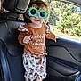Madilynn is registered to the contest to win money with this photo: child, toddler, sunglasses, car_interior, seat, barefoot, clothing, patterned_pants, brown_top, window, greenery, sunlight, smile, curly_hair, cute, playful, indoor, vehicle, portrait, casual