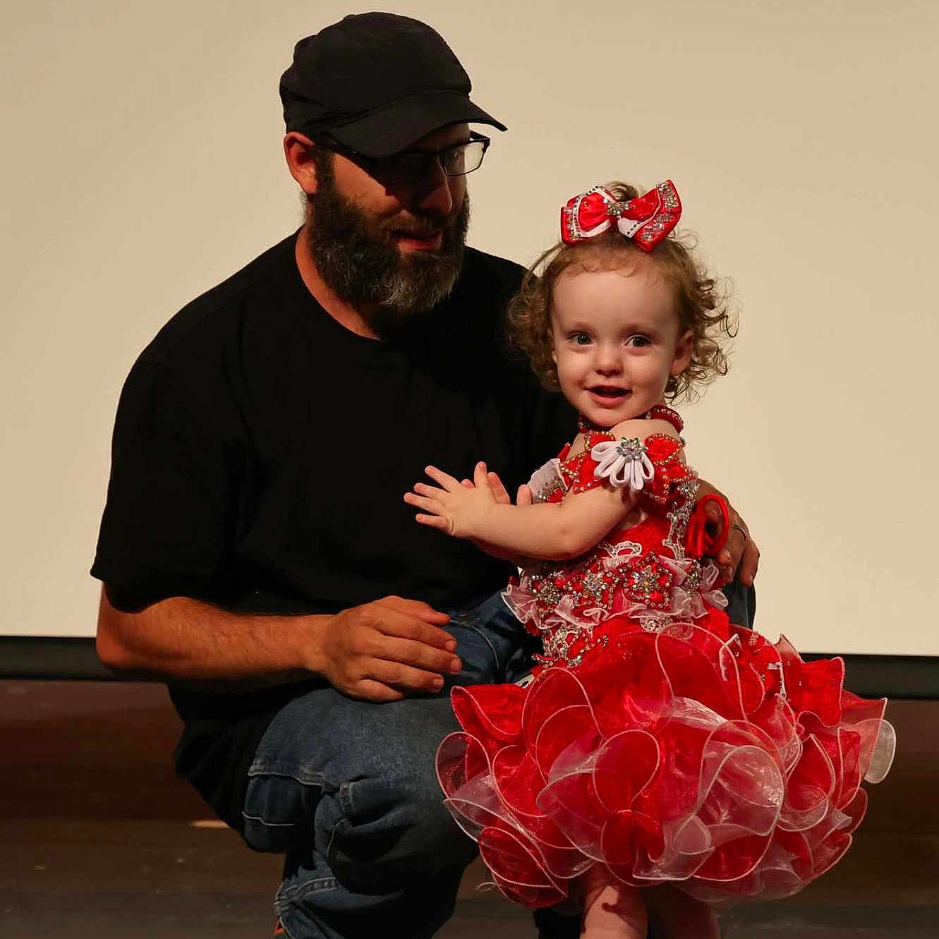 Madilynn joined the competition — help win amazing prizes! affection, beard, black_shirt, black_shoes, bow, cap, child, curly_hair, dance, family, glasses, indoor, jeans, man, performance, red_dress, smile, stage, toddler, white_socks