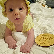 Raelynn is registered to the contest to win money with this photo: baby, infant, yellow_bonnet, yellow_clothing, white_blanket, wooden_plaque, milestone, two_months, lying_down, bedroom, soft_lighting, curious_expression, close_up, person, child, cute, indoors, portrait, newborn, hands