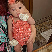 Gabriella joined the competition — help win amazing prizes! baby, infant, child, portrait, sitting, held, face, wide_eyed, looking_at_camera, flower_headband, coral_dress, floral_clothing, mittens, socks, adult, indoor, mosaic_floor, wooden_door, home, cute