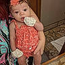 baby, infant, child, portrait, sitting, held, face, wide_eyed, looking_at_camera, flower_headband, coral_dress, floral_clothing, mittens, socks, adult, indoor, mosaic_floor, wooden_door, home, cute