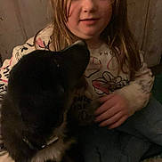 Loki is registered to the contest to win money with this photo: child, dog, indoor, carpet, casual_clothing, long_hair, pet, friendship, warm_lighting, sitting, black_dog, white_paws, young_girl, holding, cute, cozy, calm, intimate, low_light, blur