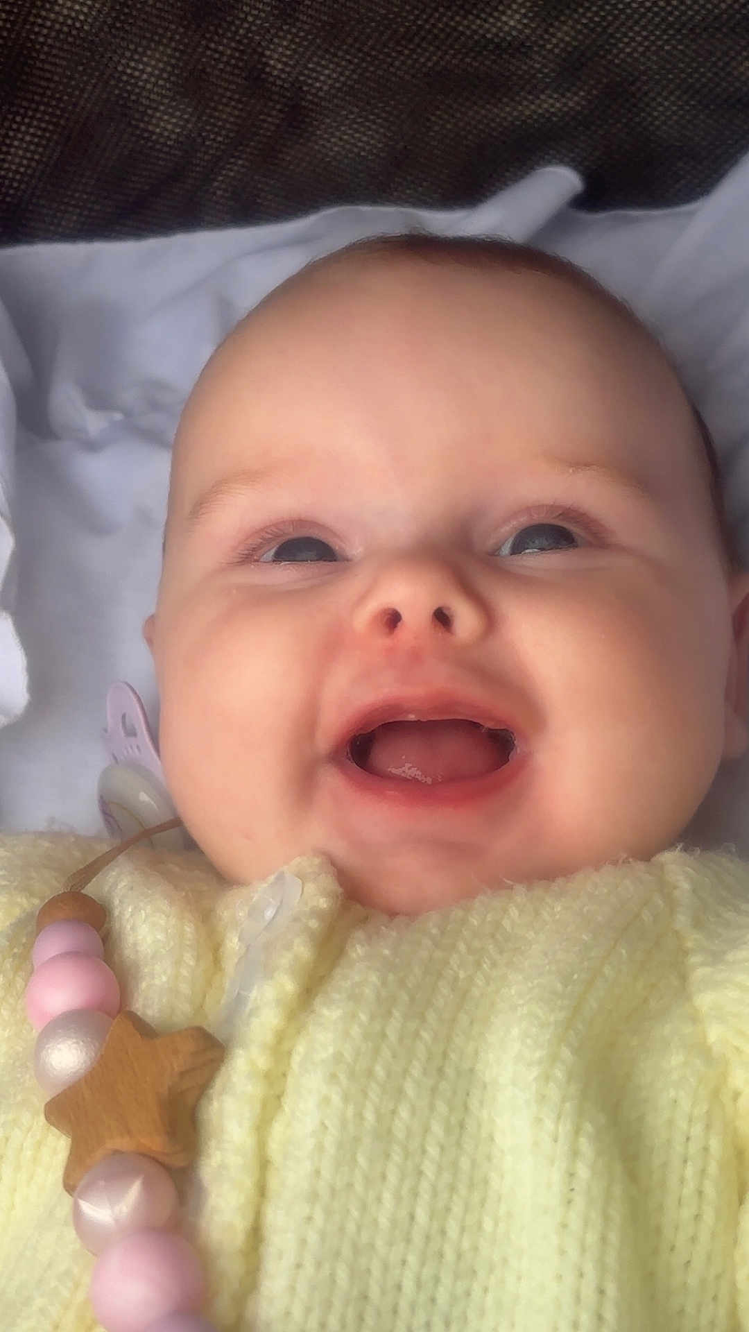 Romi is registered to the contest to win money with this photo: baby, child, smiling, face, close_up, yellow_clothing, knitted, pacifier, beads, wooden_star, happy, infant, cute, apparel, portrait, expression, indoors, soft_light, head, skin