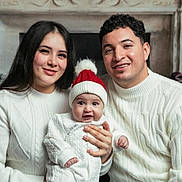 Ander is registered to the contest to win money with this photo: family, baby, child, woman, man, smile, sweater, white_clothing, hat, red_hat, indoor, holiday, christmas, fireplace, decorations, portrait, happy, seated, together, cozy