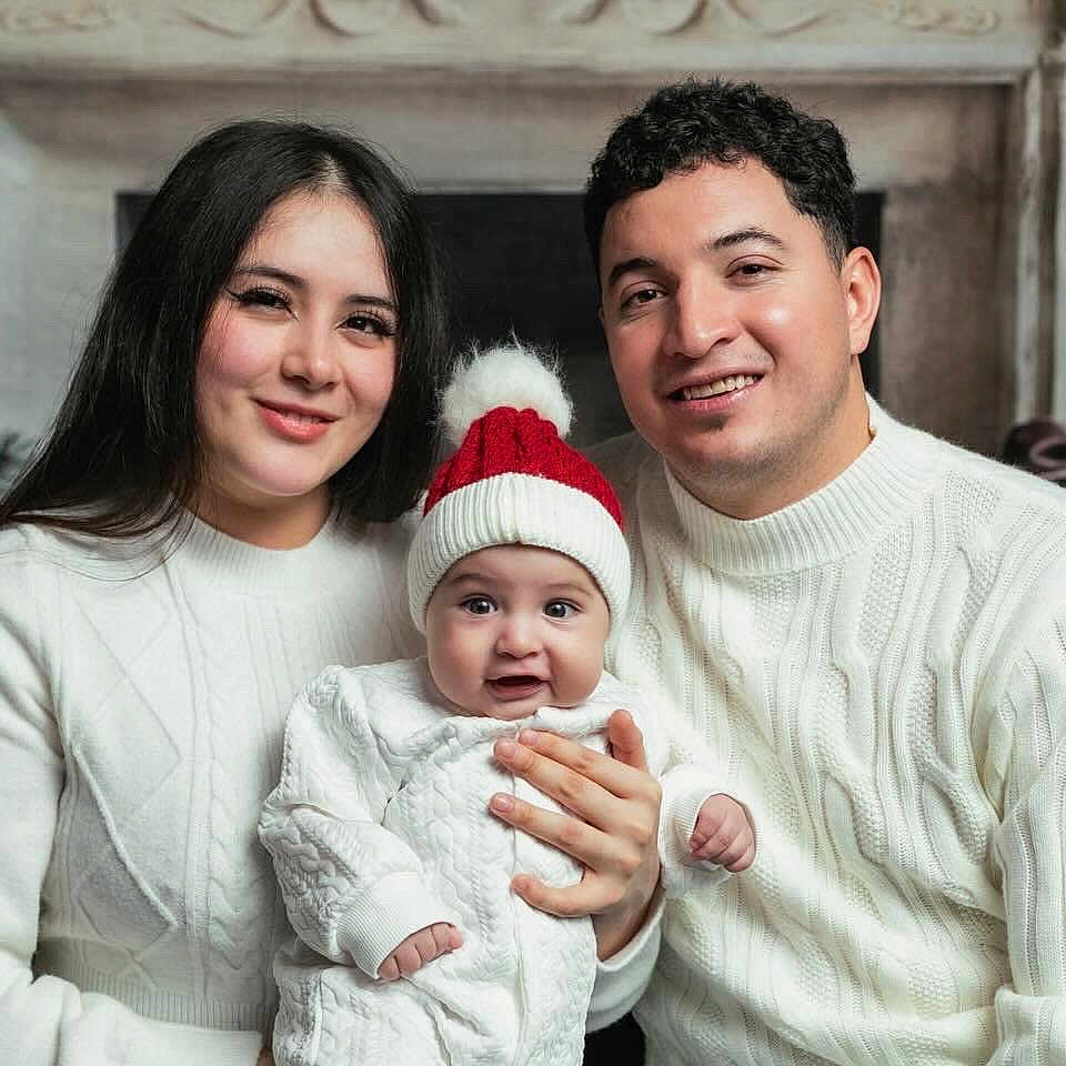 Ander is registered to the contest to win money with this photo: baby, child, christmas, cozy, decorations, family, fireplace, happy, hat, holiday, indoor, man, portrait, red_hat, seated, smile, sweater, together, white_clothing, woman