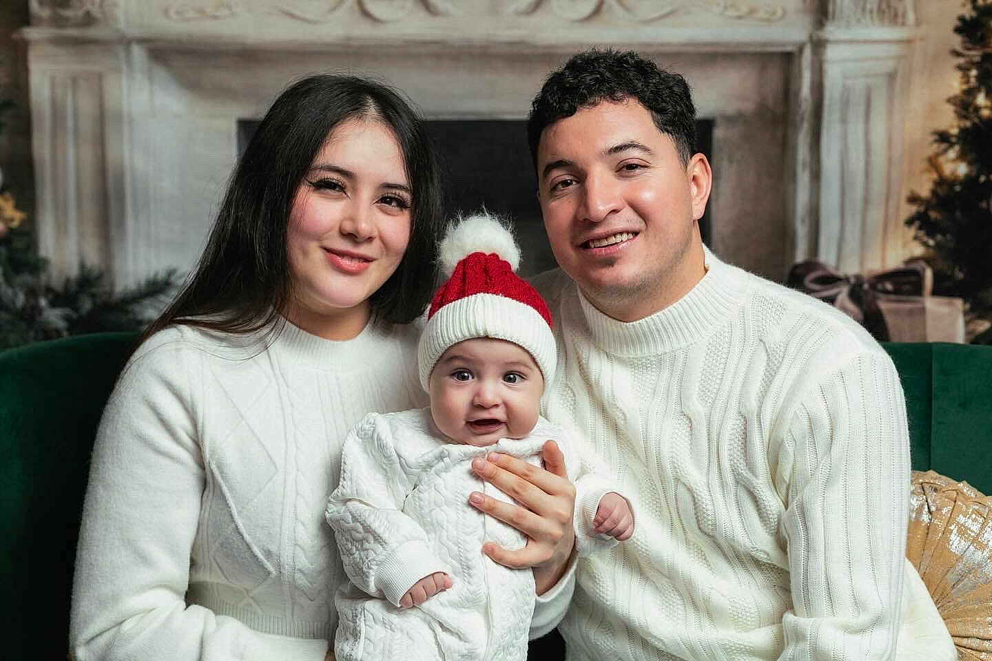 Ander is registered to the contest to win money with this photo: family, baby, child, woman, man, smile, sweater, white_clothing, hat, red_hat, indoor, holiday, christmas, fireplace, decorations, portrait, happy, seated, together, cozy