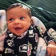 Nayeli is registered to the contest to win money with this photo: baby, smiling, blanket, onesie, happy, infant, face, closeup, child, cute, cozy, patterned_clothing, hand, lying_down, indoors, soft_texture, warm_colors, portrait, expressive, young