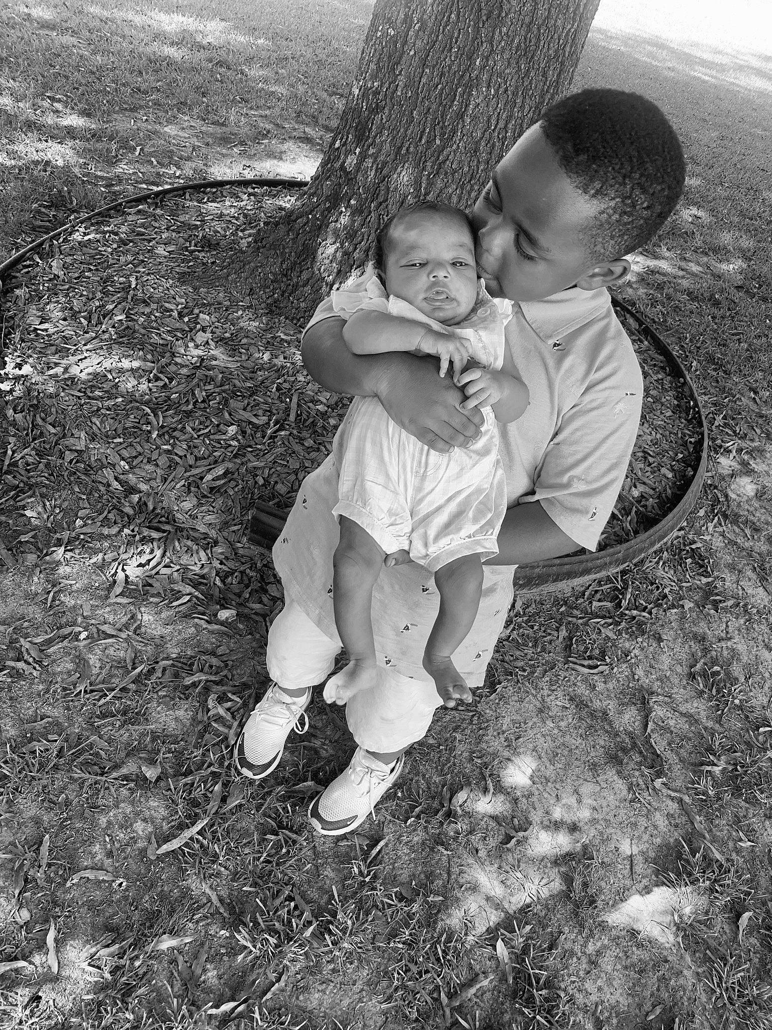 Makhi is registered to the contest to win money with this photo: baby, black_and_white, child, face, flash_photography, gesture, grass, happy, human_body, leaf, leg, monochrome, monochrome_photography, people_in_nature, person, plant, shorts, sitting, style, toddler