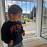 child, toddler, sweatshirt, jeans, window, open_window, daylight, sunlight, indoor, balcony, railing, smiling, happy, casual_clothing, portrait, young_child, curly_hair, side_view, playing, home