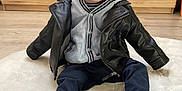 Eden participe au concours pour gagner de l'argent avec cette photo : toddler, child, leather_jacket, hoodie, sneakers, blue_eyes, smiling, sitting, rug, indoor, wooden_furniture, floor, happy, cute, portrait, casual_clothing, young_child, person, shoe, playful
