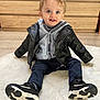 toddler, child, leather_jacket, hoodie, sneakers, blue_eyes, smiling, sitting, rug, indoor, wooden_furniture, floor, happy, cute, portrait, casual_clothing, young_child, person, shoe, playful