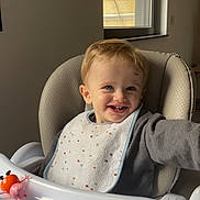 Eden a rejoint le concours — aidez-le/la à gagner de superbes lots ! toddler, child, high_chair, smiling, bib, toy, window, indoor, face, sweater, tray, plastic, light, coca_cola_sign, happy, person, cute, young_child, furniture, plaything