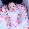 baby, infant, pink_dress, cushion, floral_pattern, stroller, heart_emoji, cute, child, portrait, indoors, soft_lighting, sleepy, small_hands, clothing, head, face, newborn, resting, comfort