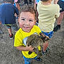 child, boy, bunny, animal, pet, yellow_shirt, outdoor, dirt_ground, people, casual_clothing, shorts, sneakers, cute, happy, smiling, crowd, festival, family, fun, summer