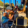 child, man, carousel, amusement_park, toy_car, giraffe, steering_wheel, sunlight, outdoor, cap, sunglasses, smile, happy, person, ride, summer, play, fun, family, vacation