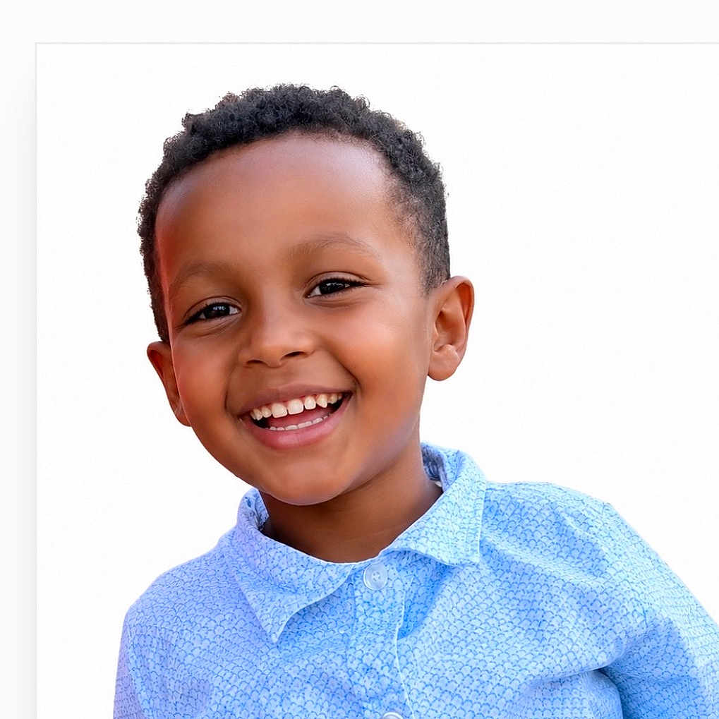 Eliab is registered to the contest to win money with this photo: child, boy, smiling, happy, face, portrait, curly_hair, blue_shirt, casual_clothing, white_background, teeth, eyes, head_and_shoulders, cute, young, person, cheerful, outdoor_light, skin, expression