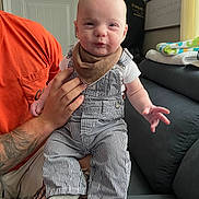 Wesley joined the competition — help win amazing prizes! baby, child, person, overalls, bib, tattoo, hand, couch, blanket, window, door, indoor, smile, expression, sitting, clothing, furniture, home, adult_hand, striped_clothing