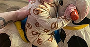 Wesley is registered to the contest to win money with this photo: baby, child, pretzel_pajamas, plush_toy, cow, yellow_rocker, indoor, floor, hand, person, foot, carpet, wood_floor, child_in_background, toy, clothing, supporting_hand, expression, face, sitting