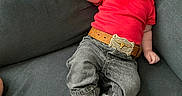 Wesley is registered to the contest to win money with this photo: baby, belt, boots, casual_clothing, child, couch, cute, fashion, happy, indoor, infant, jeans, one_person, person, portrait, red_shirt, relaxed, seated, smiling, winking