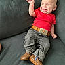 Wesley is registered to the contest to win money with this photo: baby, smiling, winking, red_shirt, belt, jeans, boots, couch, indoor, happy, infant, child, person, casual_clothing, portrait, fashion, cute, one_person, seated, relaxed