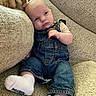 baby, child, denim_overalls, socks, couch, cushion, blanket, indoor, portrait, person, infant, relaxing, comfortable, soft_furniture, clothing, head, face, seated, cozy, cute