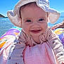 Isabelle joined the competition — help win amazing prizes! baby, child, smile, hat, sunhat, inflatable, water, lake, outdoor, sky, blue_sky, happy, face, person, summer, clothing, pink_blanket, nature, reaching, closeup