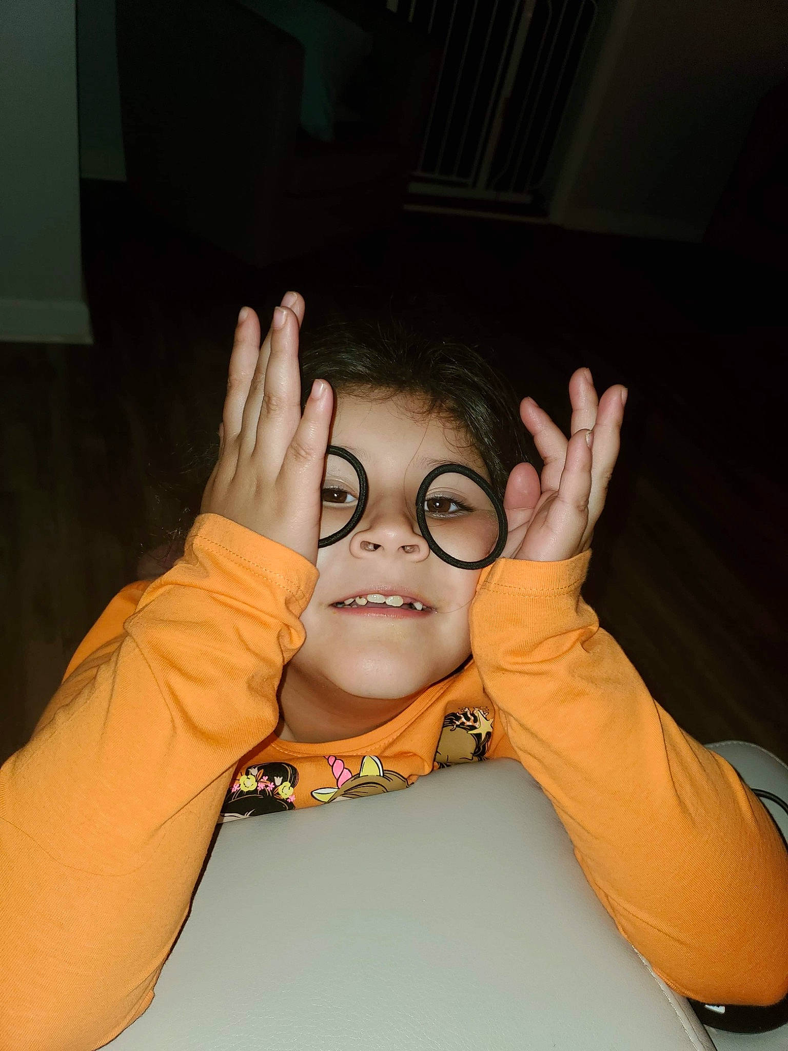 Ava is registered to the contest to win money with this photo: arm, cheek, child, eyelash, eyewear, finger, flash_photography, fun, gesture, hand, happy, hearing, nail, person, sign_language, sitting, sleeve, smile, thumb, vision_care