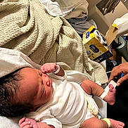 Harlem is registered to the contest to win money with this photo: newborn, baby, infant, sleeping, hospital, hospital_bed, blanket, white_clothing, onesie, swaddling, wristband, ankle_band, adult_hand, portrait, indoors, medical, birth, family, peaceful, close_up