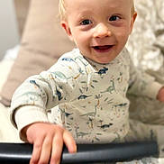 Diego participe au concours pour gagner de l'argent avec cette photo : bed, blanket, child, closeup, cozy, cute, dinosaur_print, face, hand, happy, indoors, light_blond_hair, pajamas, person, playful, sitting, smiling, soft, toddler, young_child