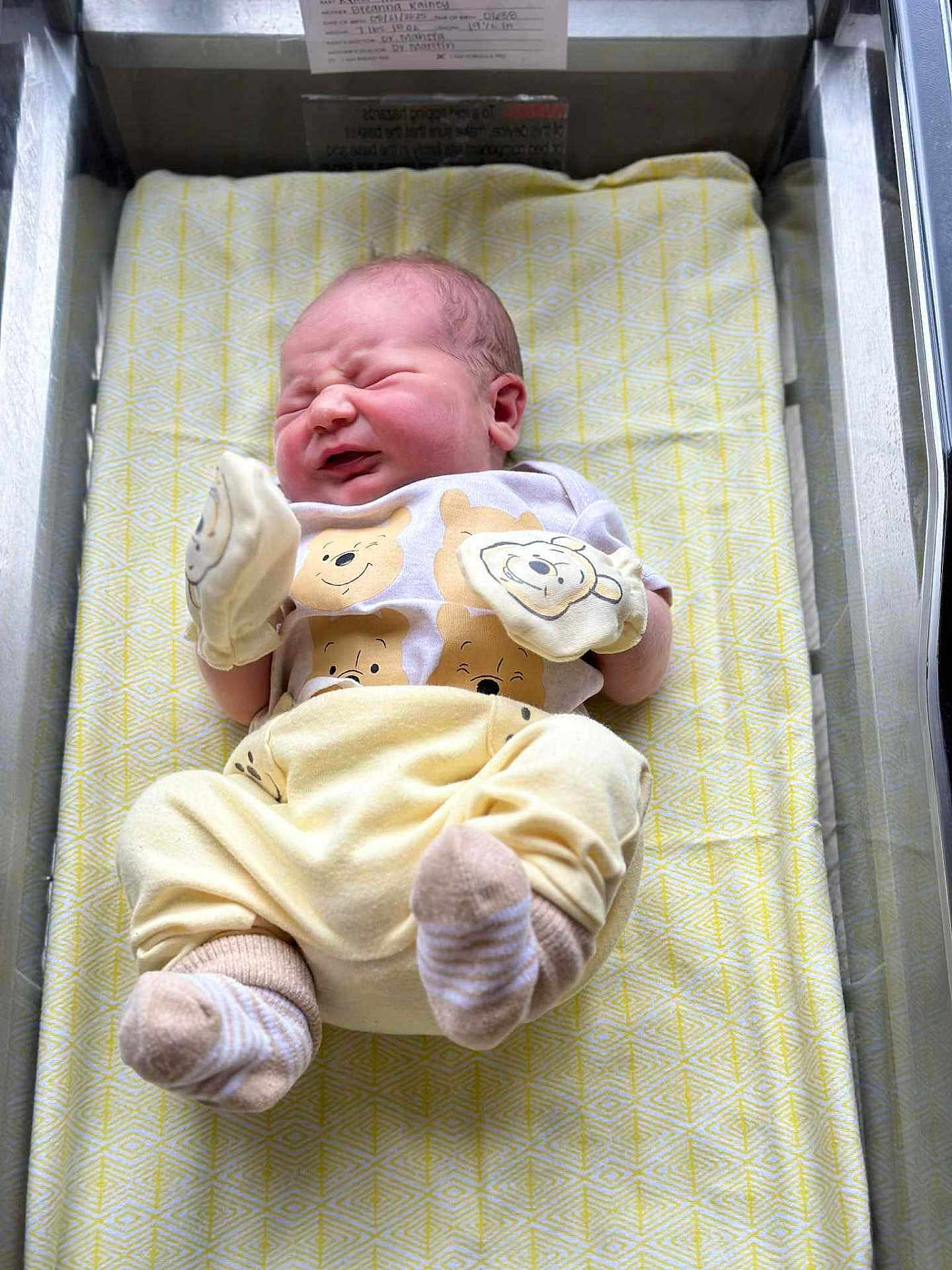 Ryker joined the competition — help win amazing prizes! newborn, baby, infant, hospital, bassinet, crib, clothing, mittens, yellow, cute, face, sleepwear, person, bed, blanket, pattern, soft, toddler, hospital_room, cute_outfit