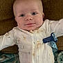 Zayden is registered to the contest to win money with this photo: baby, infant, onesie, white_clothing, duck_print, cushion, brown_background, blue_tag, smiling, face, head, lying_down, blanket, soft_texture, cute, child, closeup, indoors, person, newborn