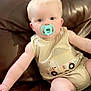 baby, pacifier, romper, truck_design, couch, leather, child, infant, sitting, cute, soft_lighting, indoor, young, face, footwear, white_shoes, buttoned_clothing, plush, skin, portrait