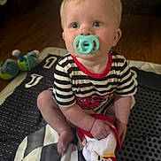 Zayden is registered to the contest to win money with this photo: baby, blanket, carpet, child, curious, cute, face, floor, foot, hand, indoor, infant, pacifier, person, plush_toy, red_trim, sitting, striped_clothing, toy, young_child