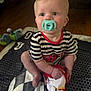 baby, blanket, carpet, child, curious, cute, face, floor, foot, hand, indoor, infant, pacifier, person, plush_toy, red_trim, sitting, striped_clothing, toy, young_child