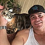 Princesa is registered to the contest to win money with this photo: man, cat, pet, smile, cap, watch, tank_top, arm, indoor, plant, pot, flower_arrangement, furniture, carpet, hand, face, resting, content, casual, portrait