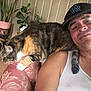 Princesa joined the competition — help win amazing prizes! man, cat, indoor, smile, cap, tank_top, couch, floral_pattern, potted_plants, flowers, home, relaxed, calico_cat, pet, furniture, portrait, happy, animal, person, casual
