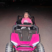 Nallely joined the competition — help win amazing prizes! child, toddler, toy_car, pink, hoodie, night, headlights, gravel_road, smile, happy, outdoor, vehicle, small_wheels, dark_background, person, play, cute, portrait, driving, fun