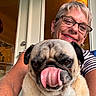 animal, closeup, cute, dog, door, face, glasses, happy, indoor, light, person, pet, playful, portrait, pug, smile, striped_shirt, tongue, warm_tone, woman