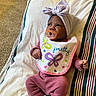 baby, infant, pacifier, bib, pink_clothing, headwrap, striped_blanket, carpet, lying_down, cute, indoors, child, newborn, socks, cozy, portrait, colorful, patterned, soft, peaceful