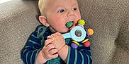 Augustin participe au concours pour gagner de l'argent avec cette photo : baby, background_blur, blue_eyes, chewing, child, colorful_toy, couch, cozy, cute, face, hand, indoor, infant, overalls, play, plush_toy, seated, soft_furniture, striped_shirt, toy