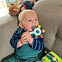 baby, background_blur, blue_eyes, chewing, child, colorful_toy, couch, cozy, cute, face, hand, indoor, infant, overalls, play, plush_toy, seated, soft_furniture, striped_shirt, toy
