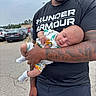 August is registered to the contest to win money with this photo: baby, car, casual_clothing, cloudy_sky, father, holding, infant, man, onesie, outdoor, parenting, parking_lot, peaceful, person, road, sidewalk, sleeping, socks, tattoo, under_armour