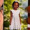 Tina is registered to the contest to win money with this photo: background_blur, bow, braids, child, cute, fashion, girl, greenery, hand, happy, outdoor, person, photo, photograph, portrait, smile, standing, summer, white_dress, young